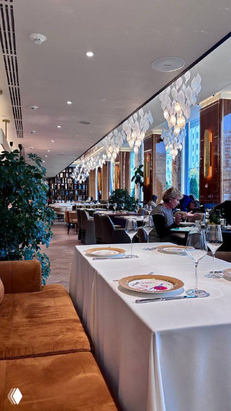 Интерьер ресторана: длинный зал с сервированными столами, люстрами и растениями — спокойная атмосферa заведения у метро Парк культуры.