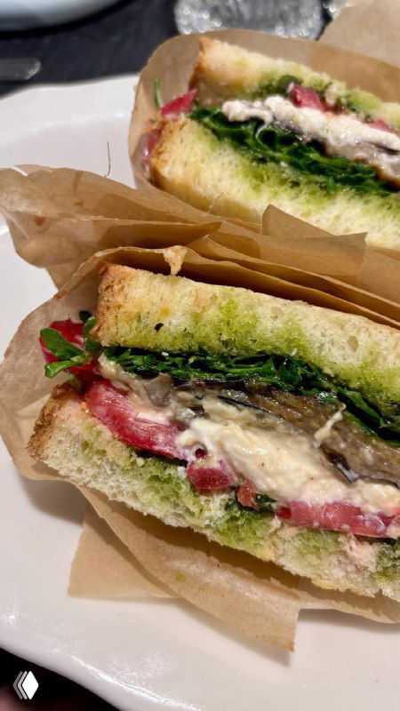 Сочное фото сендвича с баклажаном, песто и зеленью в бумажной упаковке — крупный кадр с текстурой хлеба и начинкой, на тарелке.