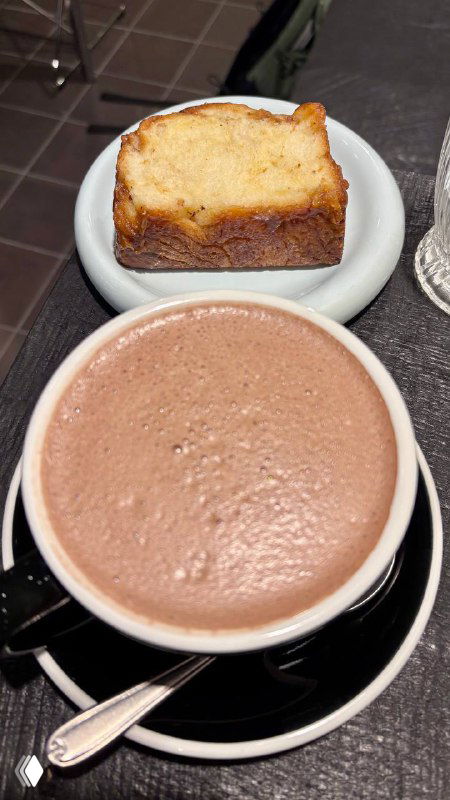 Чашка горячего напитка и кусочек кекса или бабки на блюдце — сочетание выпечки и кофе в минималистичной подаче внутри пекарни.