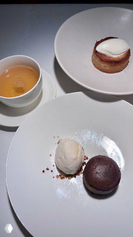 Три десерта на белых тарелках: фондан, шар мороженого и мини-пирожное рядом с чашкой — сладкая часть дегустации в ресторане.