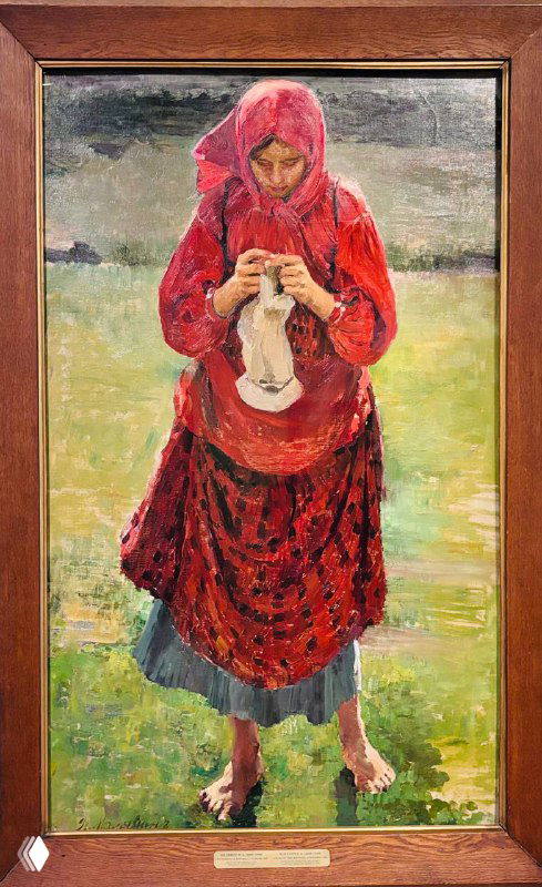 Вертикальная картина сельской женщины в красной одежде, занятой вязанием; спокойная бытовая сцена в контрасте с интенсивностью цвета на фоне.