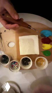 Рука держит скребок над квадратным тортом на палитре; вокруг мисочки с красками, ягодами и инструментами для украшения и росписи.