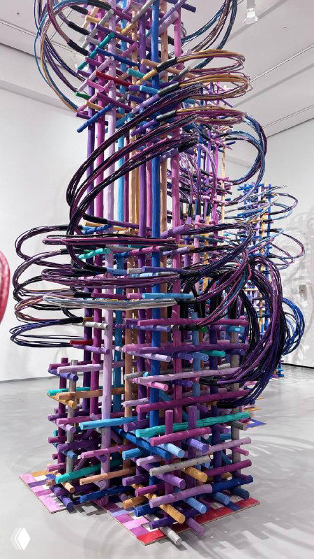 Крупная фотография или скульптурная инсталляция в виде сложной изогнутой конструкции с витиеватой формой и насыщенной фиолетово-голубой окраской в музее.