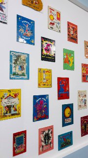 Стена, покрытая множеством цветных обложек или плакатов детских книг, аккуратно расположенных в ряд на светлой поверхности.