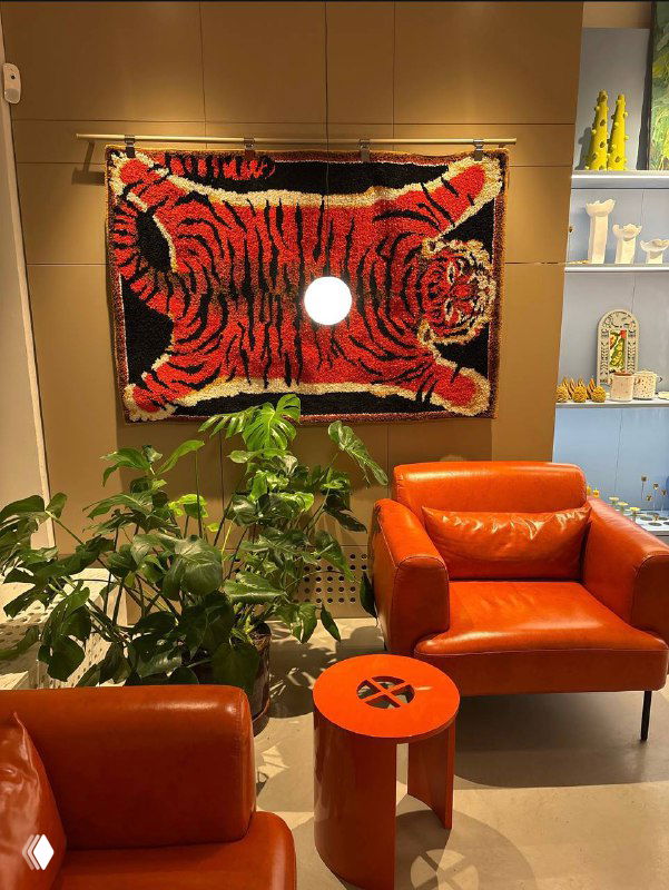 Интерьер магазина Локалы: настенный ковер с тигром, два рыжих кресла и небольшой круглый столик в уютном углу торгового пространства.