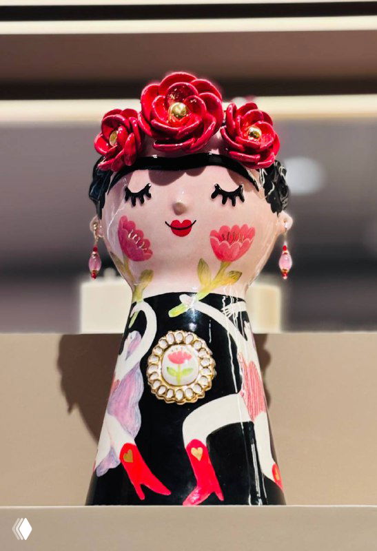 Керамическая фигурка в виде матрёшки с расписным цветочным орнаментом и аксессуарами на полке магазина Локалы — крупный план товара.