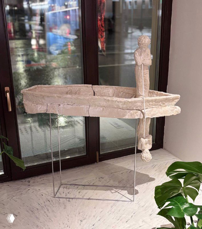 Скульптурный предмет декора на стойке у окна: светлая фактурная композиция на прозрачных подставках в витрине магазина.