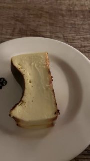 Крупный план кусочка чизкейка сверху на белой тарелке: видна пористая структура, тонкая корочка и минималистичная подача на деревянном столе.