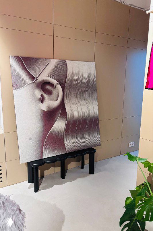 Чёрно‑белая графическая картина в интерьере магазина, под ней небольшая скамья и свободное пространство для демонстрации арт‑объектов.