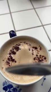 Крупный план чашки с взбитой пеной напитка Леччезе: кремовая текстура и тёмная посыпка на поверхности, видна ложка.