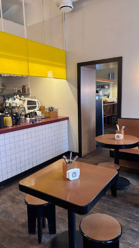 Интерьер кафе ТОТО: жёлтые верхние шкафчики, кофейная стойка и деревянные столы с табличкой заведения на столе