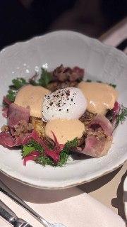 Тарелка с закуской: яйцо пашот, соус и зелень, ломтики мяса и травы, аккуратная подача в ресторане в нейтральных тонах.