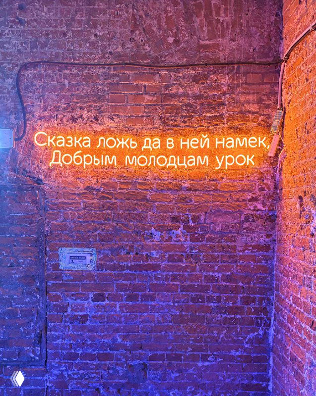 Неоновая цитата на кирпичной стене в тёплом освещении — инсталляция с текстом из сказки на фоне выставочного пространства Винзавода.