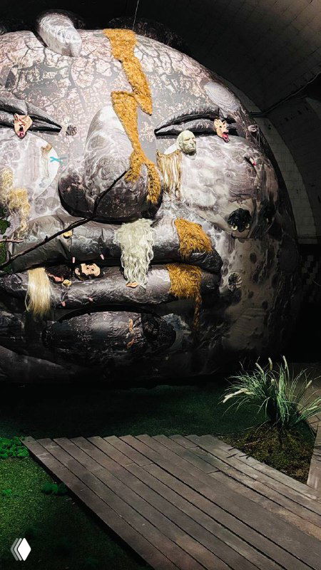 Большая округлая инсталляция с лицом и прожекторами в полутонах, часть масштабной композиции в помещении выставки на Винзаводе.