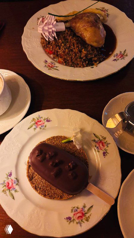 Тарелка с утиной ножкой и гречневой кашей на фарфоре в элегантной подаче, рядом кофейная чашка и приборы в ресторане «Пушкинъ».