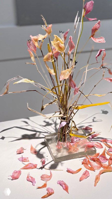 Натюрморт из стеклянных цветочных форм и опавших лепестков на белом постаменте — детализированная и хрупкая работа, имитирующая живую ботанику.