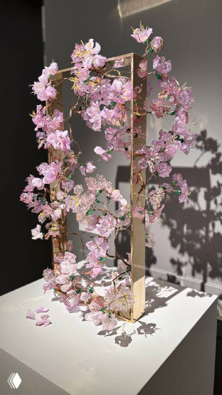 Розовые стеклянные цветы, оформленные в вертикальную рамку на постаменте, тонкая и декоративная композиция из прозрачного и цветного стекла в зале галереи.