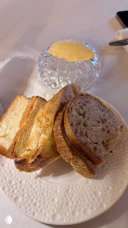 Комплимент от ресторана Шануар: ассорти из хлеба и порция их фирменного масла на белой тарелке — подача и текстура хлеба на фото.