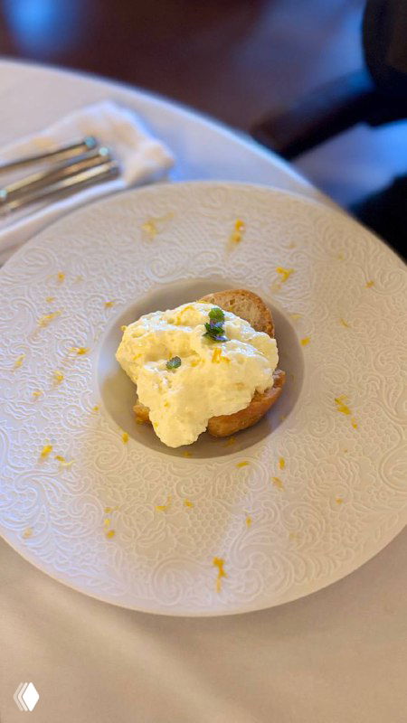 Небольшая закуска на белой тарелке в ресторане Шануар: лаконичная подача крема или паштета на хлебной основе с мелкими деталями сервировки.