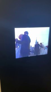 Крупный план инсталляции в ГЭС‑2: на переднем плане маленький вертикальный экран с движущимися фигурами, вокруг тёмный выставочный зал и силуэты посетителей.