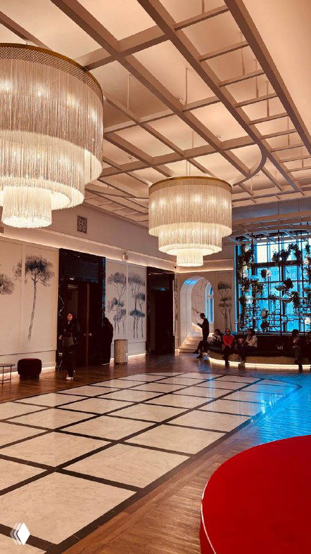 Просторный вестибюль кинотеатра с контрастной чёрно‑белой плиткой, большими люстрами и зоной для ожидания перед сеансом в ретро‑стиле.