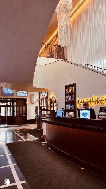 Уголок лобби с ресепшеном и полукруглой барной стойкой, полками с изданиями и тёплым освещением, характерным для исторических кинотеатров Москвы.