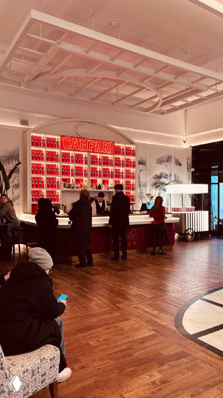 Барная зона с посетителями у стойки, деревянный паркет и полки с предметами декора, создающие живую атмосферу перед сеансом в «Художественном».