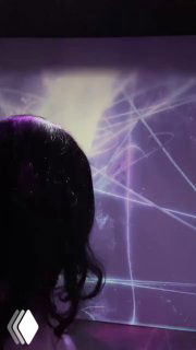 Силуэт посетителя на фоне фиолетовой проекции: светящиеся пересекающиеся линии и геометрические узоры иммерсивной инсталляции в зале.