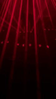 Интенсивный кадр с множеством вертикальных красных лазерных лучей, образующих геометрический узор в пространстве зала выставки.
