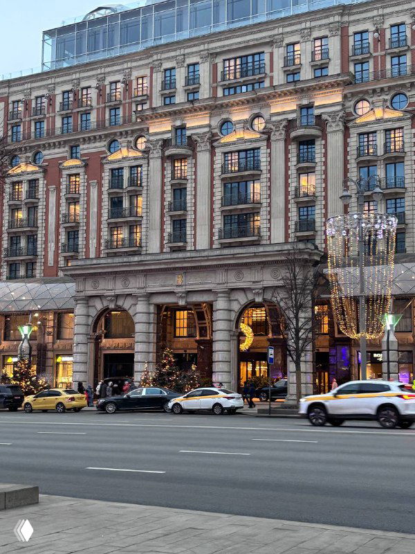 Фасад отеля Carlton и главный вход в ресторан Sartoria Lamberti на Тверской улице в Москве, городской трафик и такси на дороге.