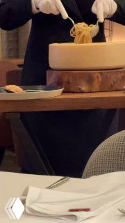 Подача спагетти cacio e pepe в сырной головке: повар извлекает пасту из пармезановой головы у стола, демонстрация подачи блюда в ресторане.