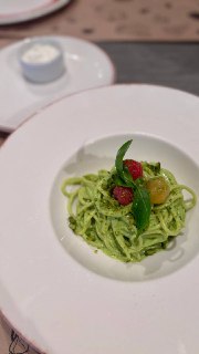 Тарелка с зелёной пастой, украшенной помидорами черри и зеленью, аккуратная сервировка на столе в ресторане.