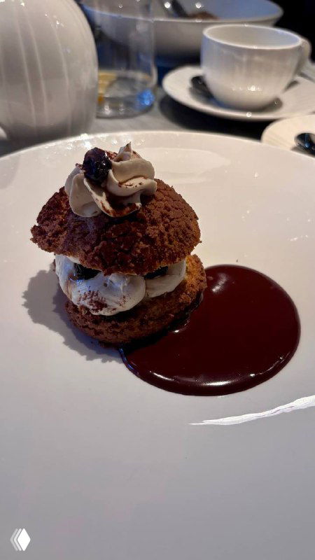 Крупный план десерта «ТирамиШу»: круглый эклер с кремовой начинкой и шоколадным соусом на белой тарелке, ресторанная подача.