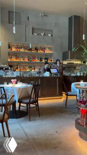 Светлый и просторный интерьер Rebecca: барная зона со стеллажами, столы и стулья, ненавязчивая ресторанная атмосфера и теплый свет.