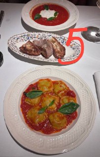 Фото пасты №5: две тарелки с томатным соусом и равиоли, а также кусочки хлеба на белой скатерти; композиция снята сверху в ресторане.