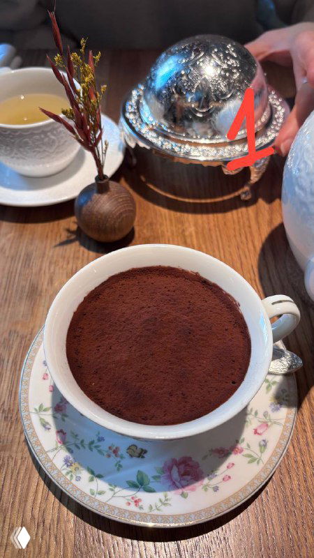 Крупный план тирамису в чашке на столе с посудой и чайником рядом; тёмный слой какао сверху, кадр из обзора десертов автора.