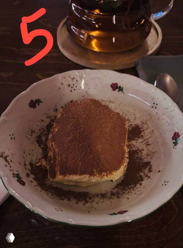 Квадратный кусок тирамису на винтажной тарелке, сверху какао, рядом чай — снимок демонстрирует классический вид десерта.