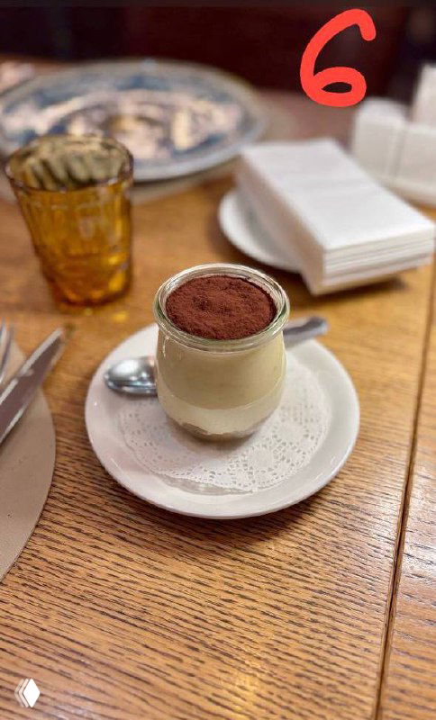 Маленькая порция тирамису в стеклянном стаканчике с ложкой на подставке, аккуратная подача в кафе, кадр обзора.