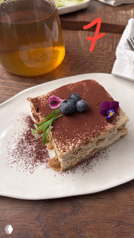 Классический прямоугольный тирамису на белой тарелке с ягодами и съедобным декором, фото демонстрирует оформление блюда.