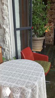 Интерьер ресторана: стол с белой кружевной скатертью, красное кресло и большое горшечное растение у окна на фоне ковра на полу.