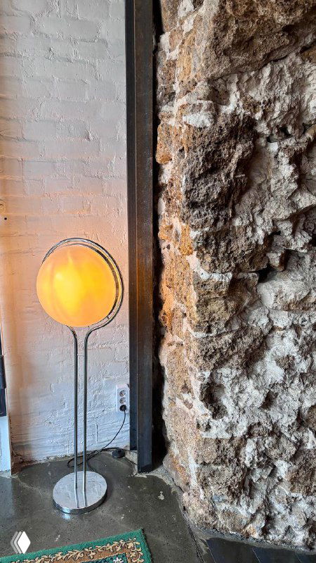 Напольный торшер у фактурной кирпичной стены и грубого каменного участка, создающие контраст текстур в интерьере ресторана.