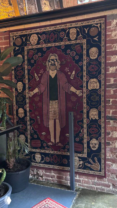 Декоративный настенный ковёр с изображением персонажа в центре, висящий на кирпичной стене — акцентный элемент в оформлении заведения.