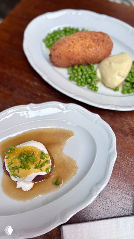 Порция с креветками или патисонами в соусе на белой тарелке и гарнир из зелёного горошка, ресторанная подача на деревянном столе.