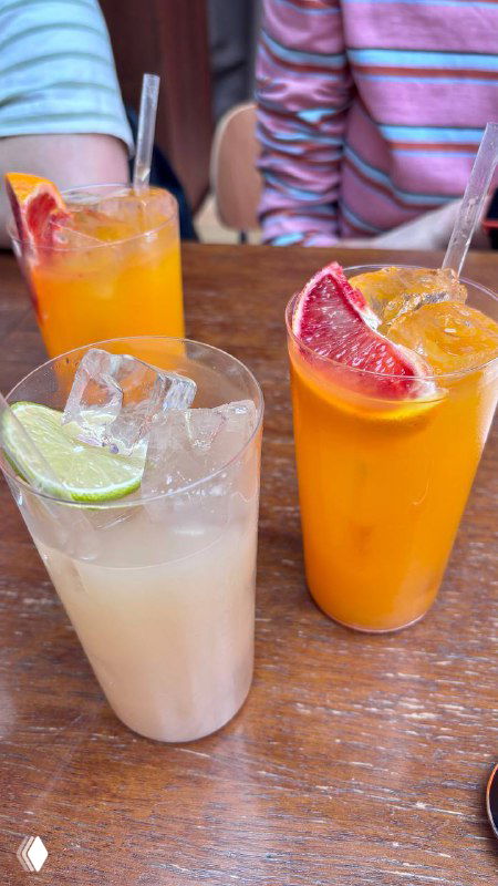 Несколько холодных напитков в стаканах разной формы на столе: яркие соки и лимонады в неформальной подаче в ресторане.