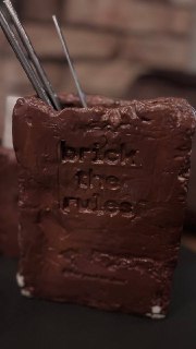 Крупный план десерта или оформления в форме кирпича с надписью «brick the rules», текстура шоколада и декоративные элементы.
