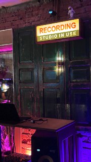 Деревянные двери с вывеской 'RECORDING STUDIO IN USE', индустриальный интерьер бара с оборудованием и разноцветной подсветкой вокруг