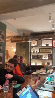 Широкий вид на барную зону с посетителями за столиками, полки с декоративными предметами и оживлённая непринуждённая обстановка