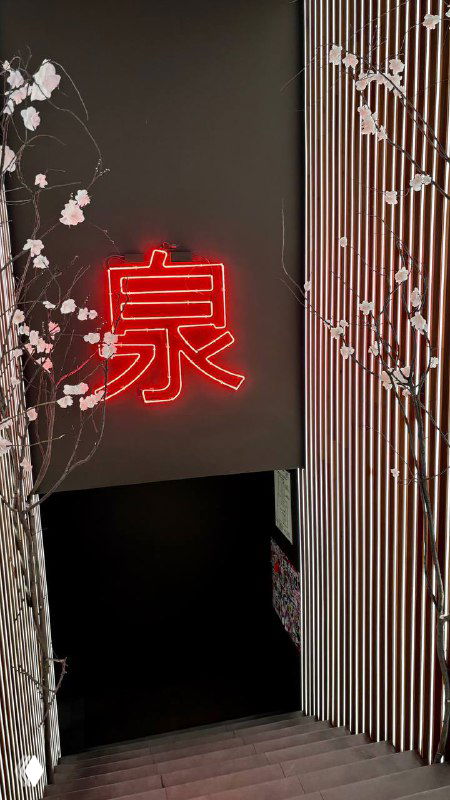 Неоновая красная вывеска с иероглифом у входа, сакуровые ветви и лестница, создающие японский антураж заведения.