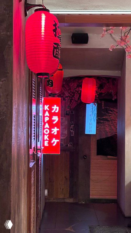 Узкий коридор с красными фонариками и неоновыми указателями караоке, создающий атмосферу ночного японского бара.