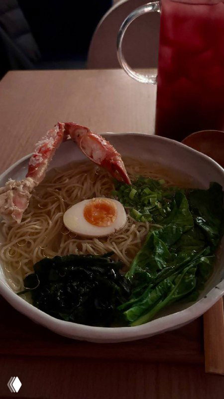 Большая миска рамена с крабом, половинкой яйца, ошпаренным шпинатом и водорослями вакаме на фоне деревянного стола.